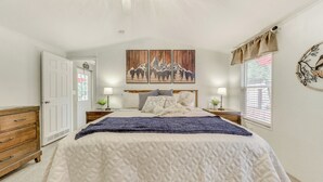 Ein Schlafzimmer mit Bett, Holzkommode und Fenster mit Jalousien.