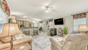 Ein geräumiges Wohnzimmer mit einer Couch, Sesseln, einem Couchtisch und einem an der Wand montierten Fernseher.