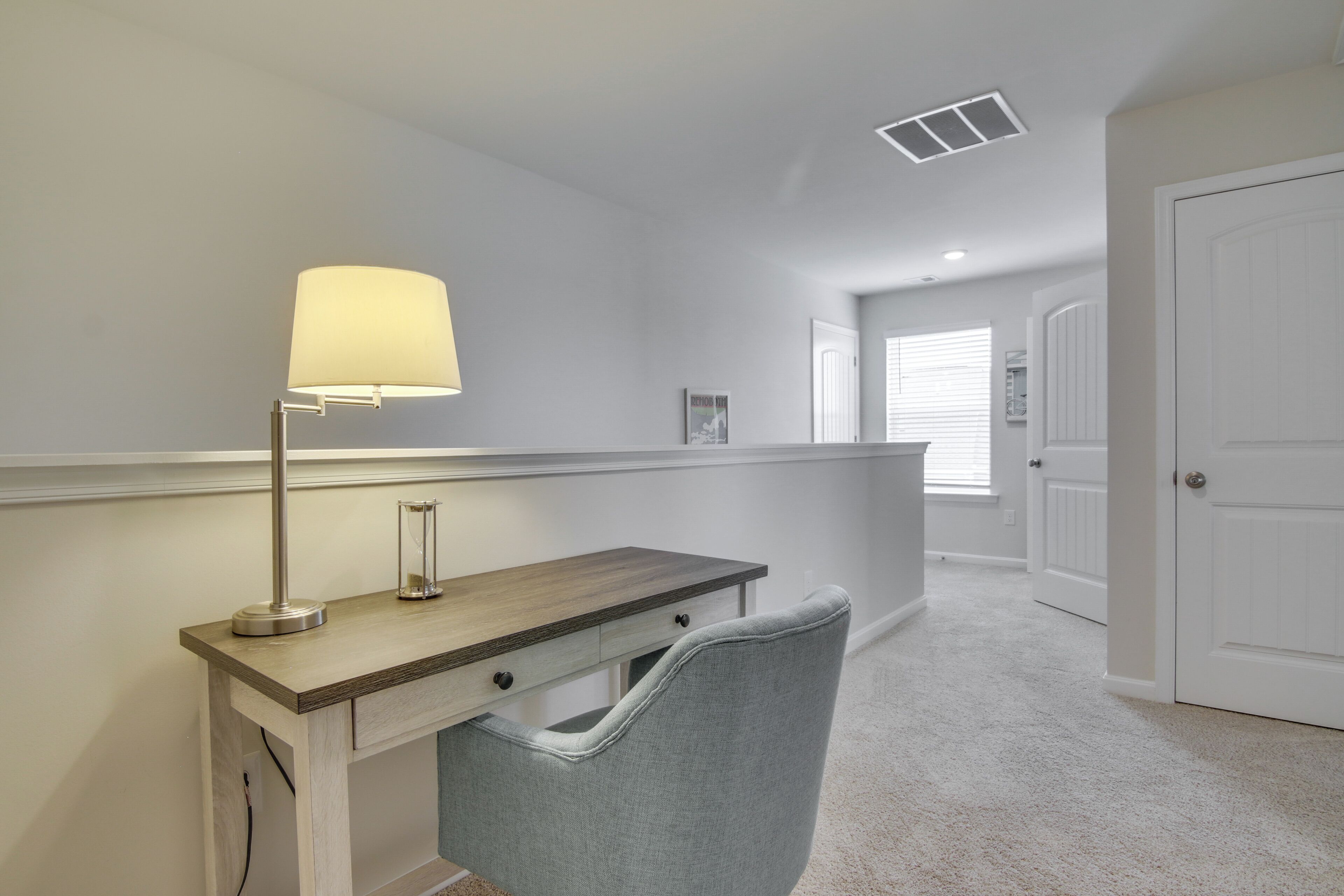 A hallway with a desk, chair, lamp, and a door.