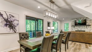 A modern dining area with a wooden table, leather chairs, and a stone fireplace. - Waynesville Cabin w/ Pickleball Court and Hot Tub (Waynesville)