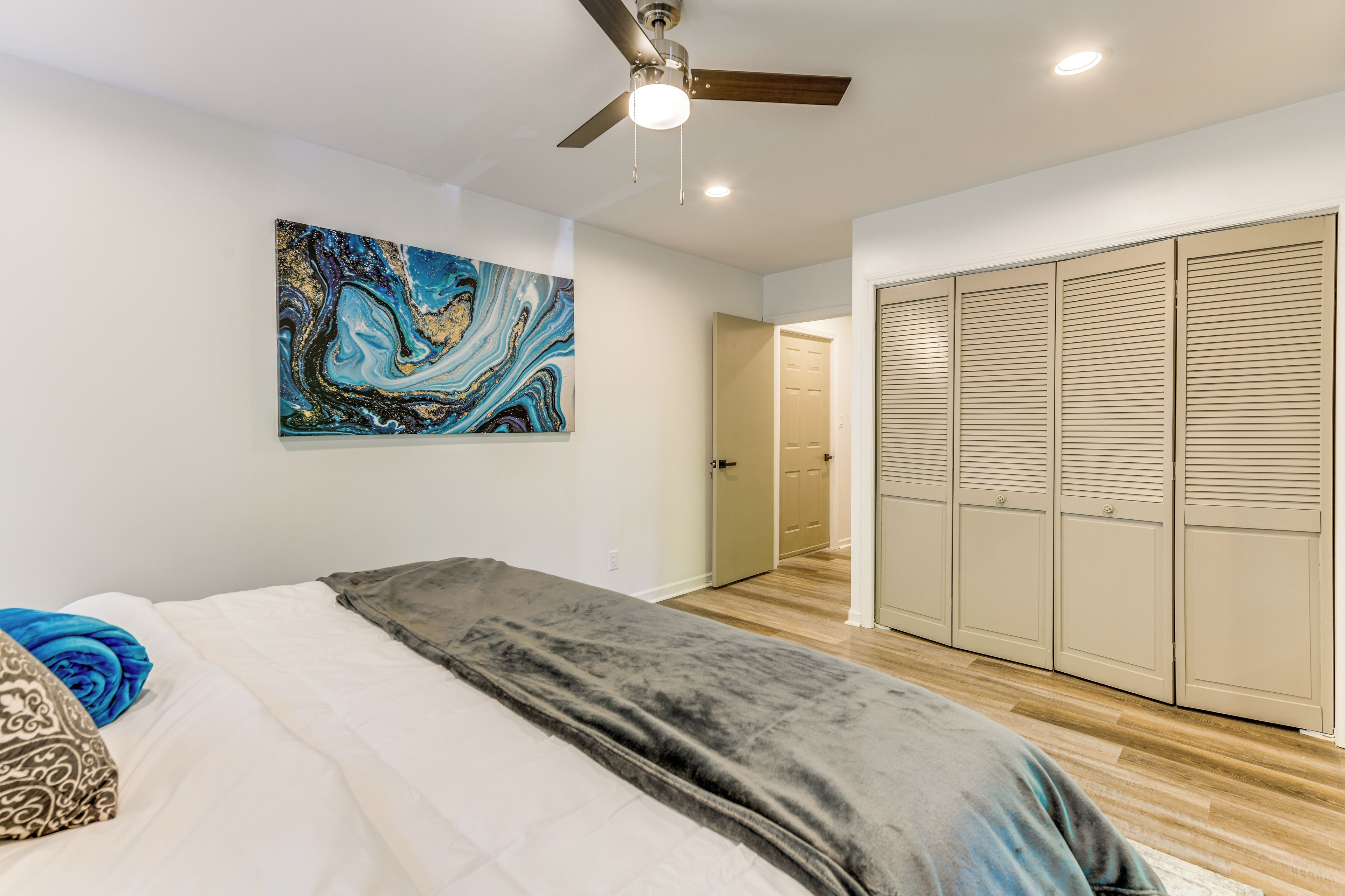 A bedroom with a bed, a ceiling fan, a wall-mounted abstract painting, and a walk-in closet.