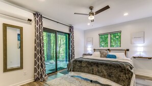 A bedroom with a large bed, a ceiling fan, and a view of the outdoors through a sliding glass door. - Waynesville Cabin w/ Pickleball Court and Hot Tub (Waynesville)