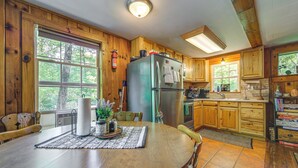 A wooden cabin kitchen with a large dining table, wooden cabinets, and a refrigerator. - Pet-friendly Creekside Cabin w/ Pool Access! (Maggie Valley)