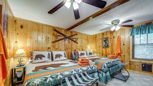 A wooden cabin bedroom with two beds, a ceiling fan, and a window with curtains. - Pet-friendly Creekside Cabin w/ Pool Access! (Maggie Valley)