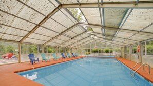 An indoor swimming pool with clear glass walls, blue chairs, and a roof structure. - Pet-friendly Creekside Cabin w/ Pool Access! (Maggie Valley)