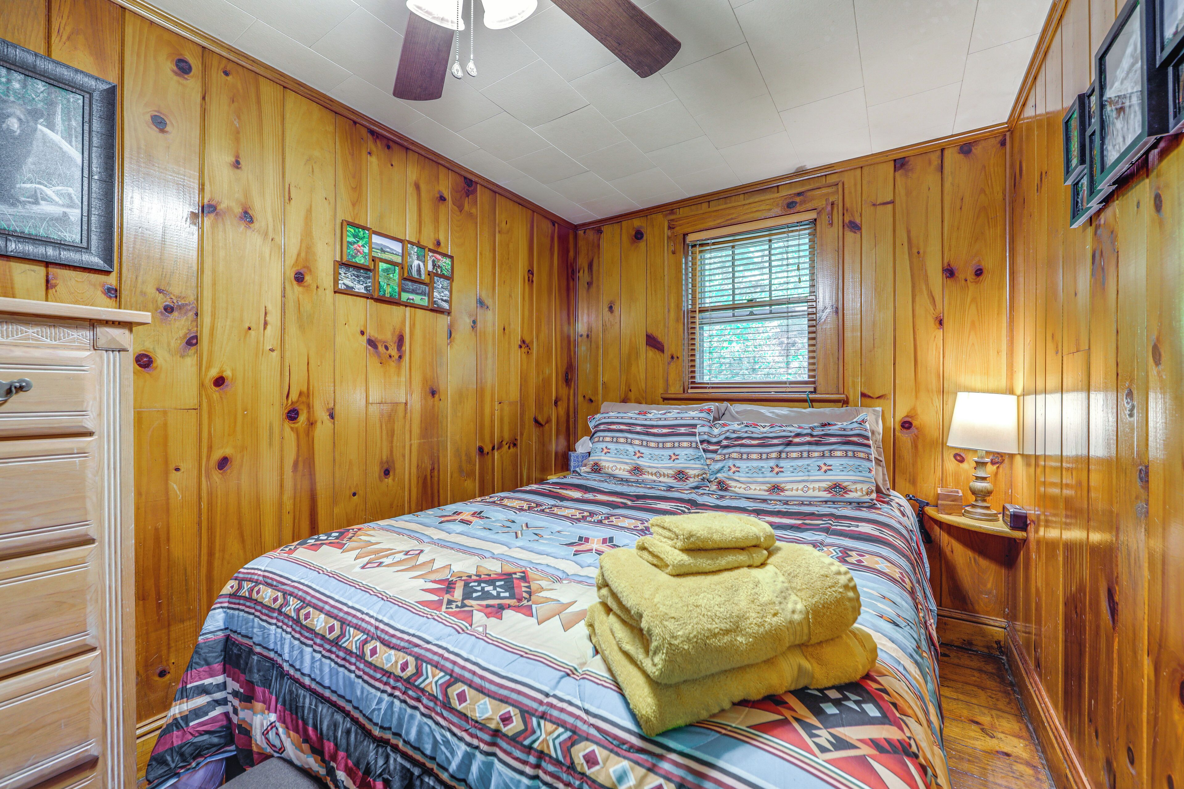 A wooden-paneled room with a bed, a dresser, and a window with blinds.