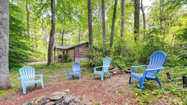 A cabin surrounded by a forest with four blue Adirondack chairs. - Pet-friendly Creekside Cabin w/ Pool Access! (Maggie Valley)