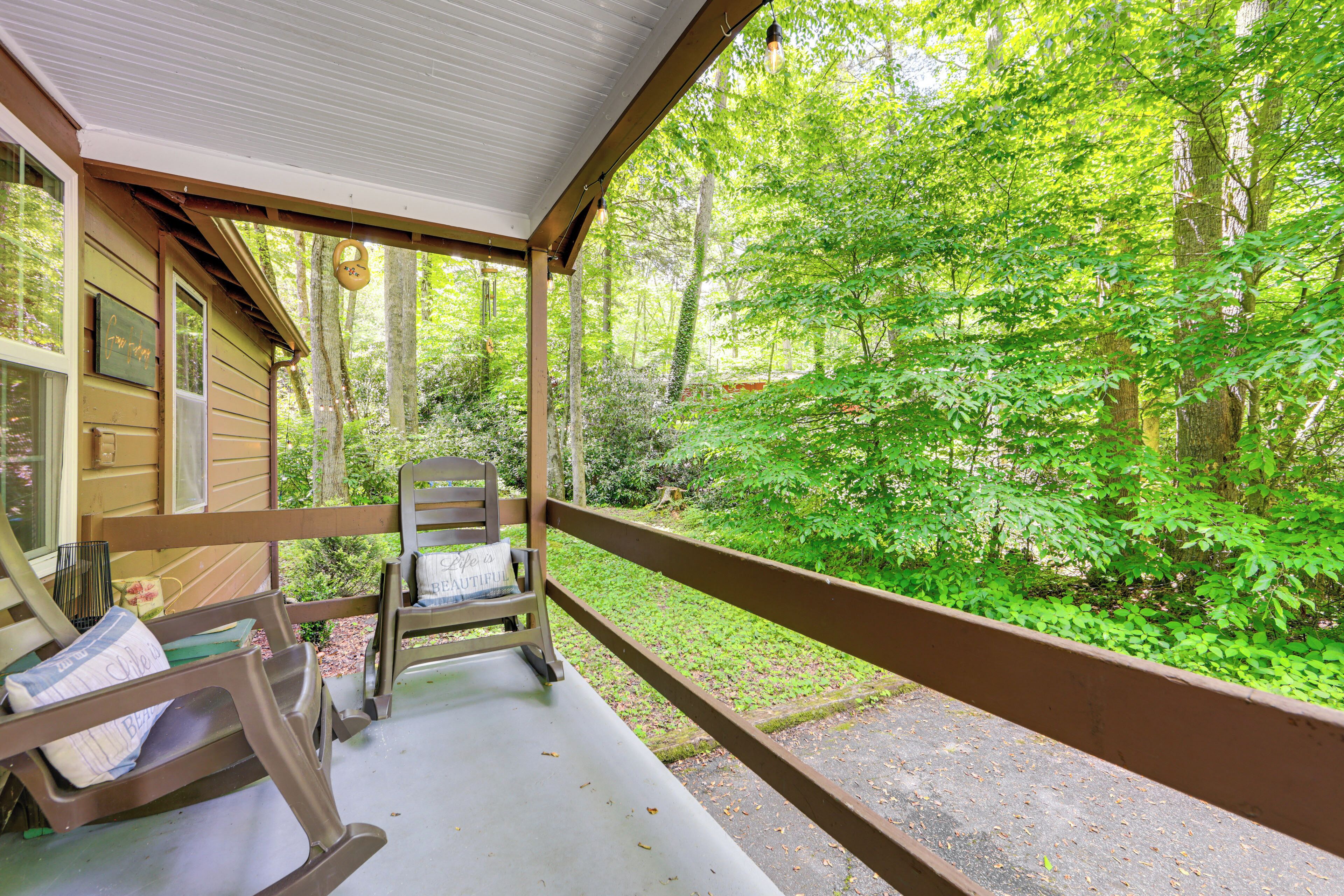 A porch with two rocking chairs, a small table, and a view of a forested area.