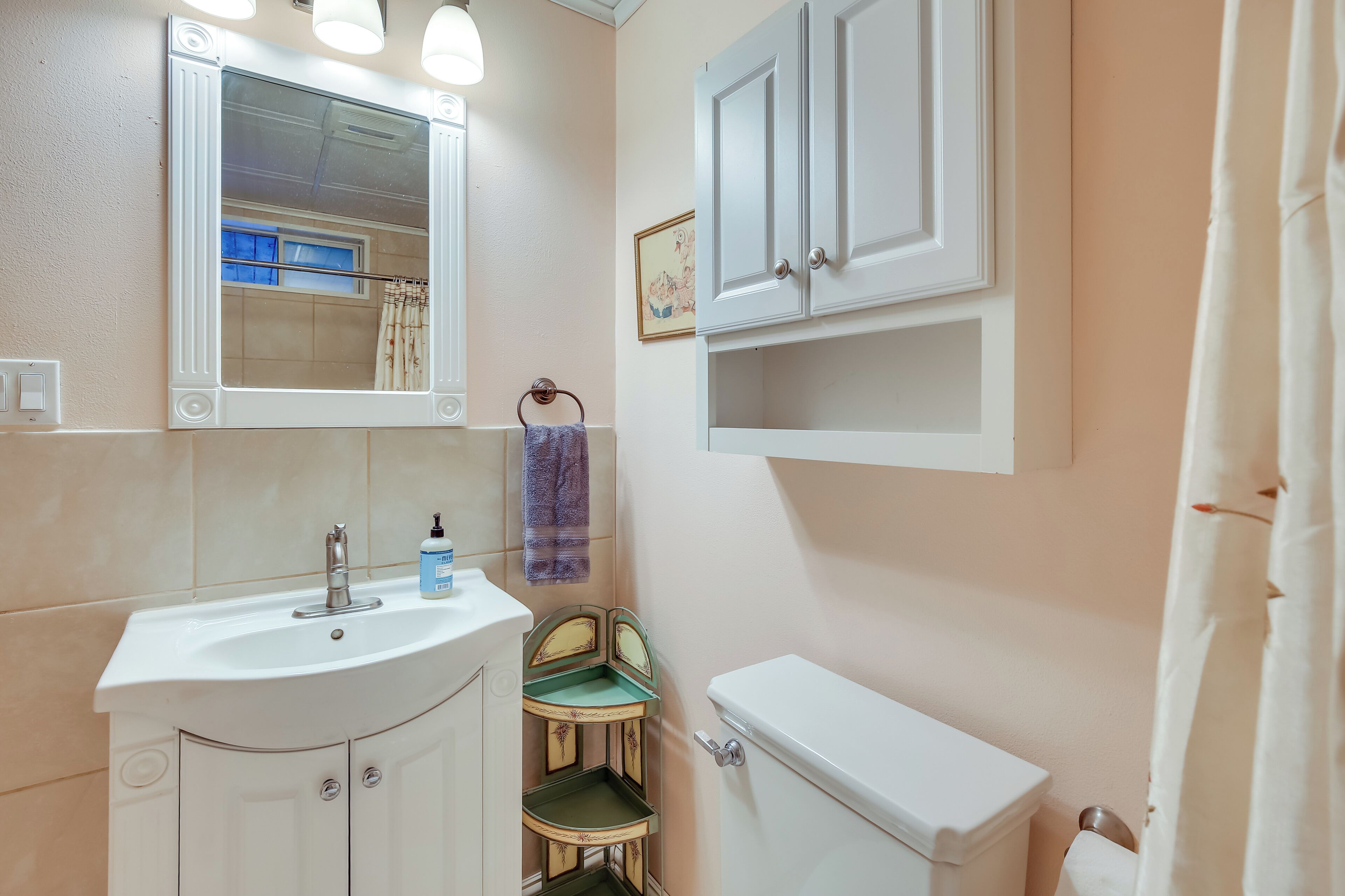 Une salle de bain équipée d’un lavabo, d’un miroir, de toilettes et d’un meuble de rangement.