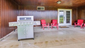 Eine überdachte Terrasse mit Grill, einem weißen Kühlschrank und roten Stühlen.
