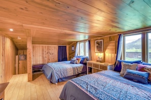 A wooden cabin room with two beds, a desk, and a window with a view.