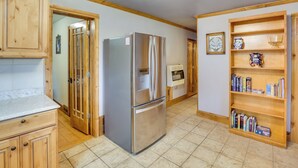 Eine Küche mit Holzausbau, einem Edelstahlkühlschrank, einem Bücherregal aus Holz und einem Fliesenboden.