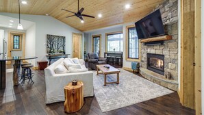 A spacious living room with a stone fireplace, wooden ceiling, and a flat-screen TV mounted above it. - Grill + Water Views: Chinquapin Resort Home (Glenville)