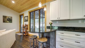 A kitchen with wooden flooring, white cabinets, a bar area with stools, and a large window with blinds. - Grill + Water Views: Chinquapin Resort Home (Glenville)