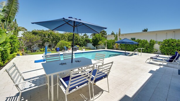 Ett område vid poolen med ett bord och stolar, en pool och parasoller.