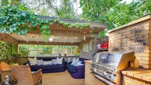 Une terrasse extérieure avec un sol en briques, un barbecue, des chaises en osier et un canapé bleu.