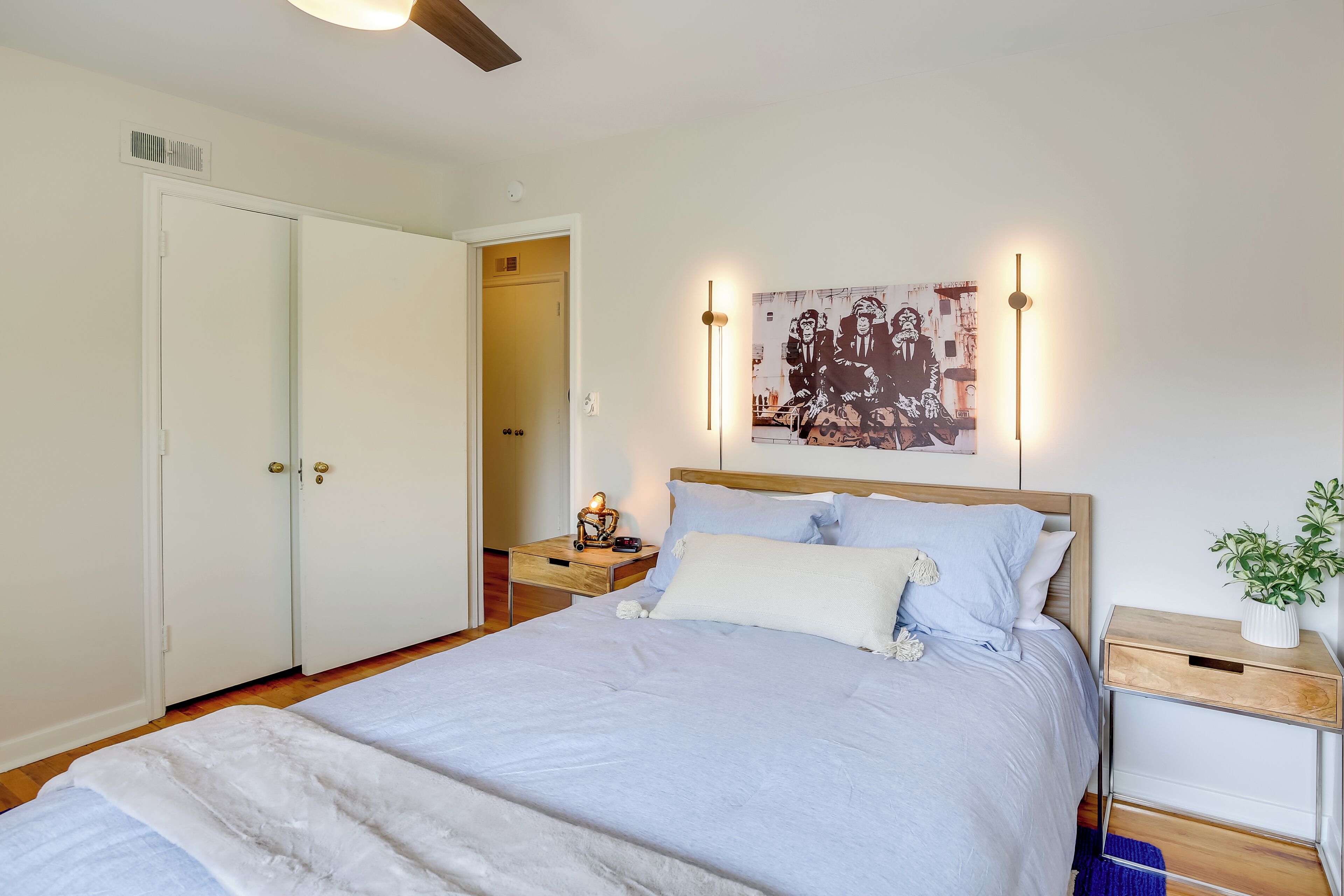 Un dormitorio con cama, mesitas de noche, lámpara de pared y una puerta.
