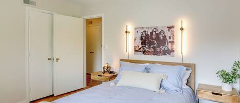 Un dormitorio con cama, mesitas de noche, lámpara de pared y una puerta.
