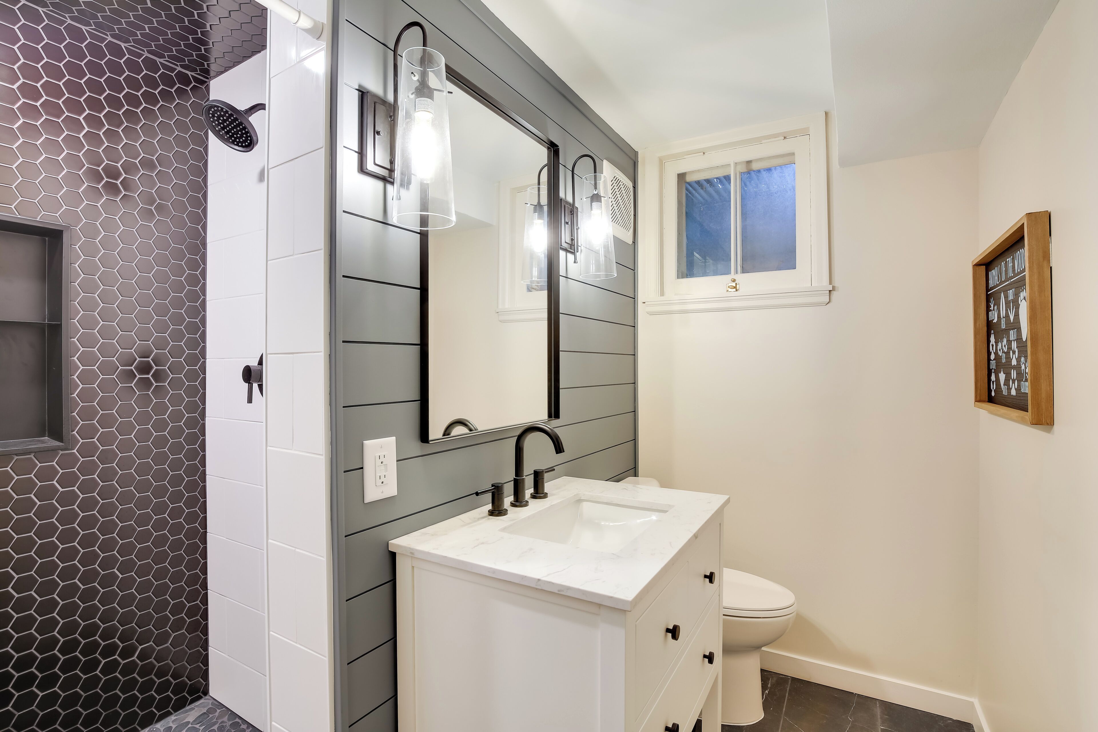 A modern bathroom with a white vanity, a large mirror, and a shower with a hexagonal tile pattern.