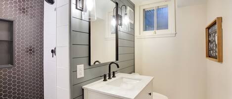 A modern bathroom with a white vanity, a large mirror, and a shower with a hexagonal tile pattern.