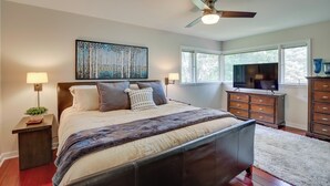 Une chambre à coucher comprenant un lit, des lampes de chevet, un ventilateur de plafond, une télévision et une commode.