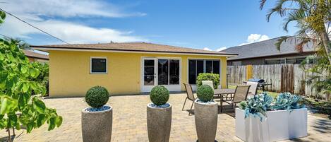 A yellow house with a patio, three tall planters with spherical topiary, and a wooden fence.