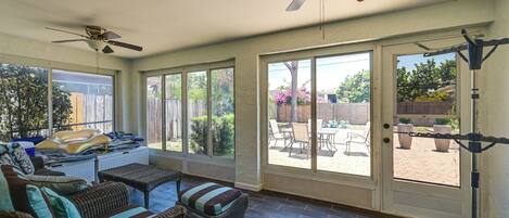 A sunlit room with wicker furniture, a ceiling fan, and a view of the backyard through large sliding glass doors.