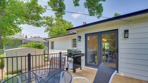 Eine überdachte Terrasse mit einem Metalltisch und -stühlen, einem Grill und einer Glastür zu einer Holzterrasse.