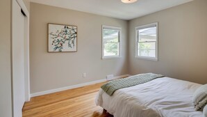 Ein Schlafzimmer mit einem Bett, zwei Fenstern, einer Deckenleuchte und einem an der Wand hängenden Bild.