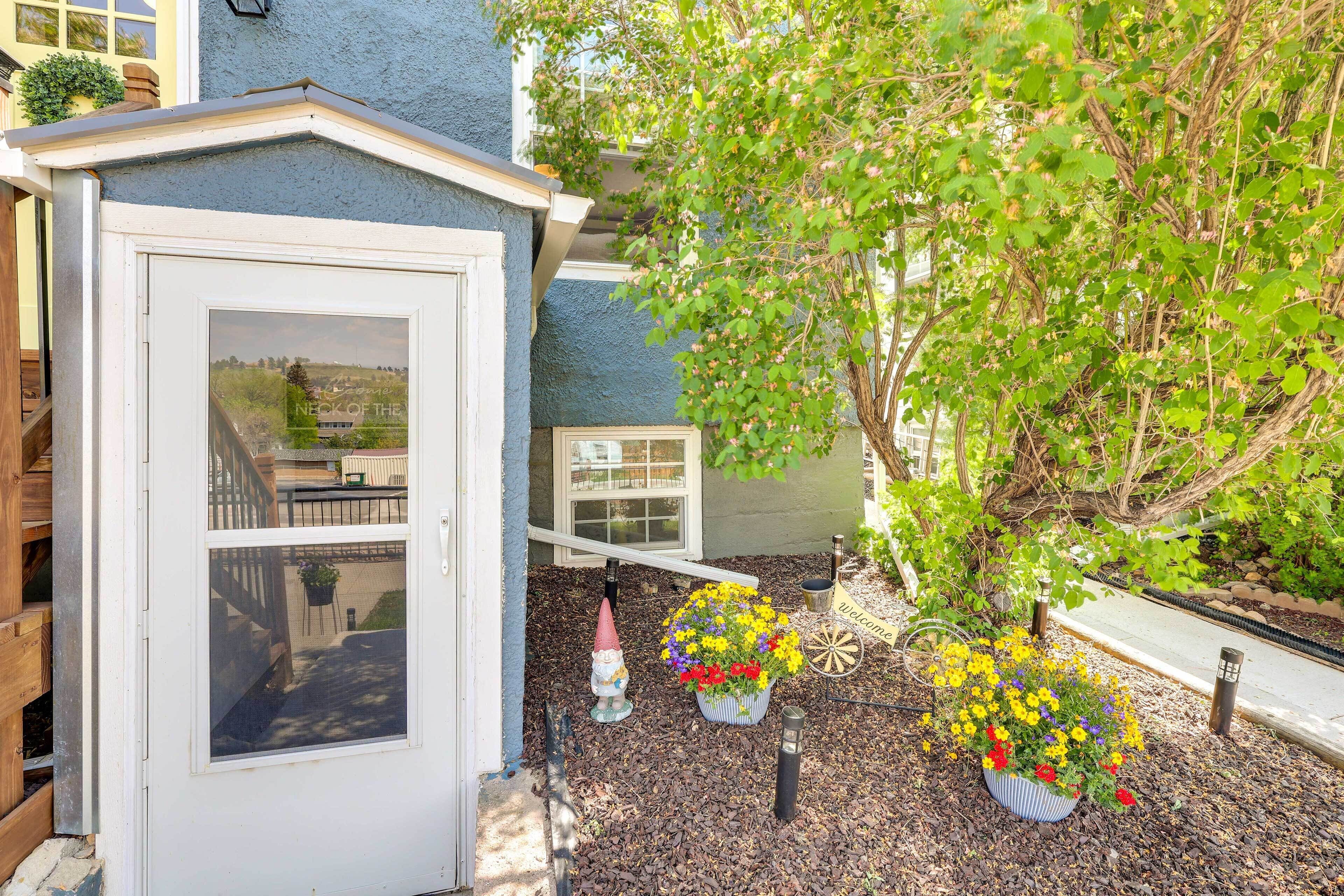 A small shed with a window, surrounded by mulch, and two flower pots with yellow and red flowers.