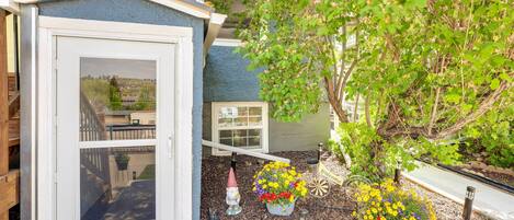 A small shed with a window, surrounded by mulch, and two flower pots with yellow and red flowers.