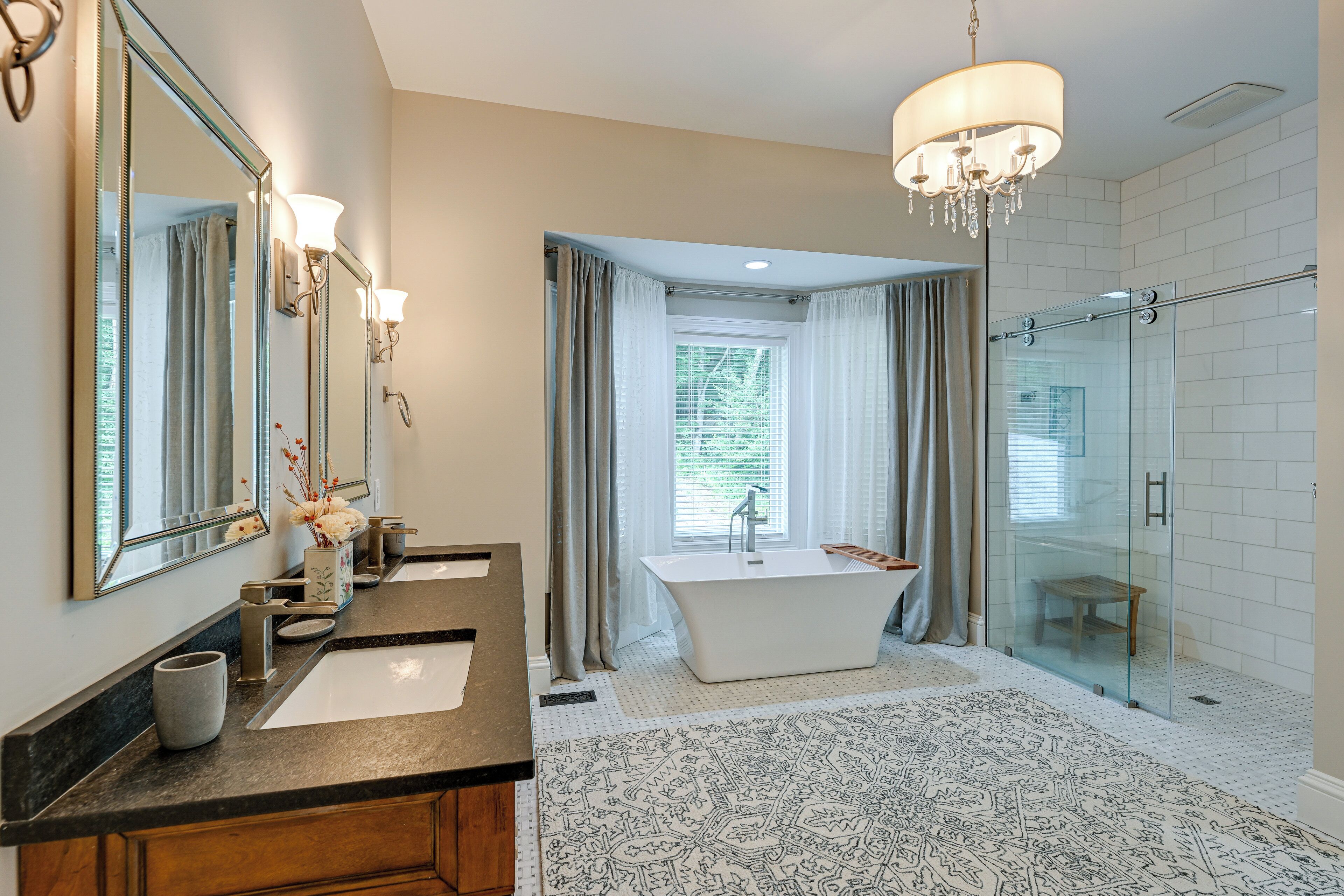 Une salle de bain moderne dotée d’un meuble-lavabo à deux vasques, d’une baignoire sur pieds, d’une douche à parois de verre et d’un lustre.