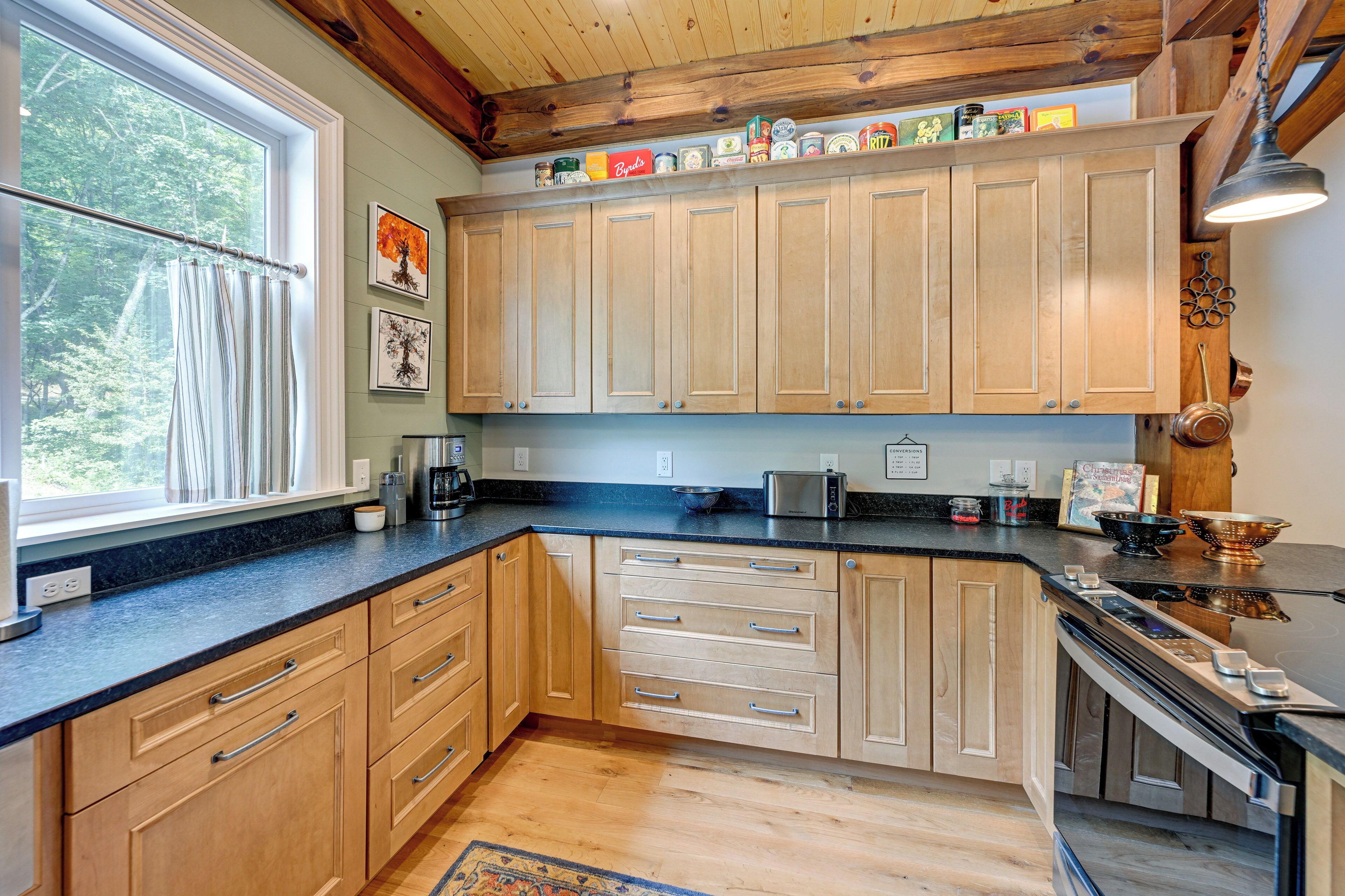 A kitchen with wooden cabinets, a black countertop, and a window with curtains.