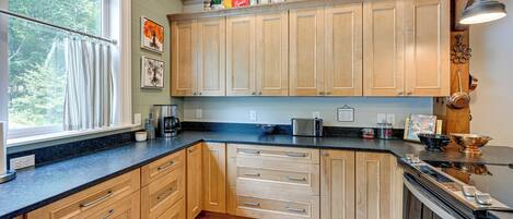 A kitchen with wooden cabinets, a black countertop, and a window with curtains.