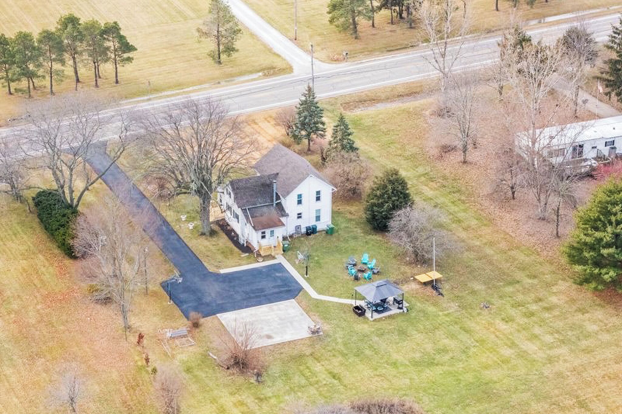 An aerial view of a house with a driveway, a lawn, and a small patio area with outdoor furniture.