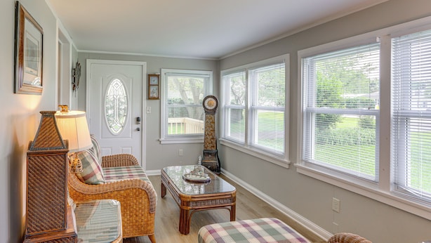 A cozy living room with wicker furniture, a glass coffee table, and large windows with blinds. - Welcoming Port Clinton Vacation Rental! (Port Clinton)