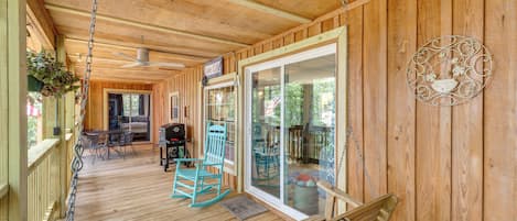 Una terraza de madera con un ventilador de techo, una mecedora y una mesa de patio.