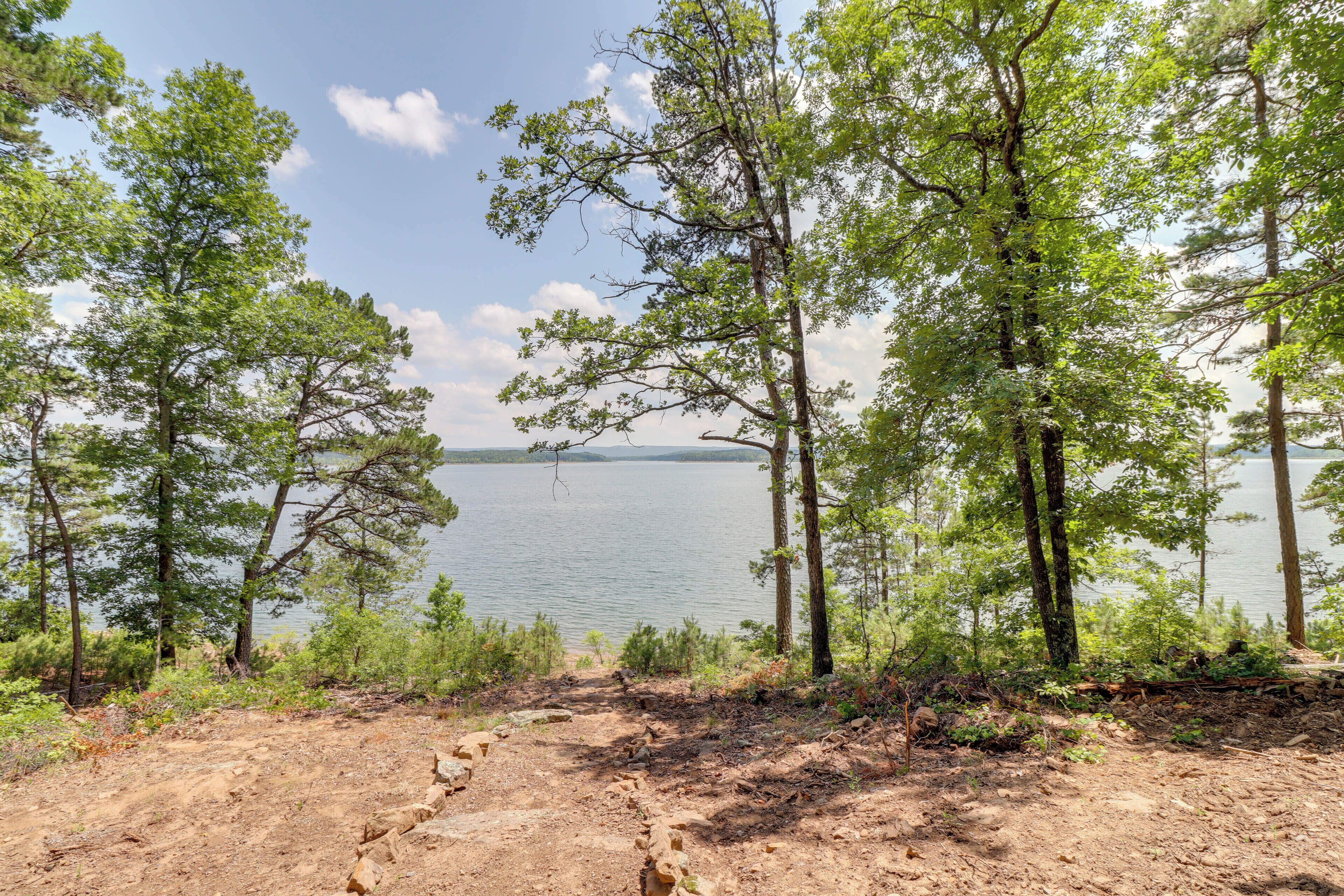 A natural landscape with a dirt path leading to a body of water, surrounded by trees.