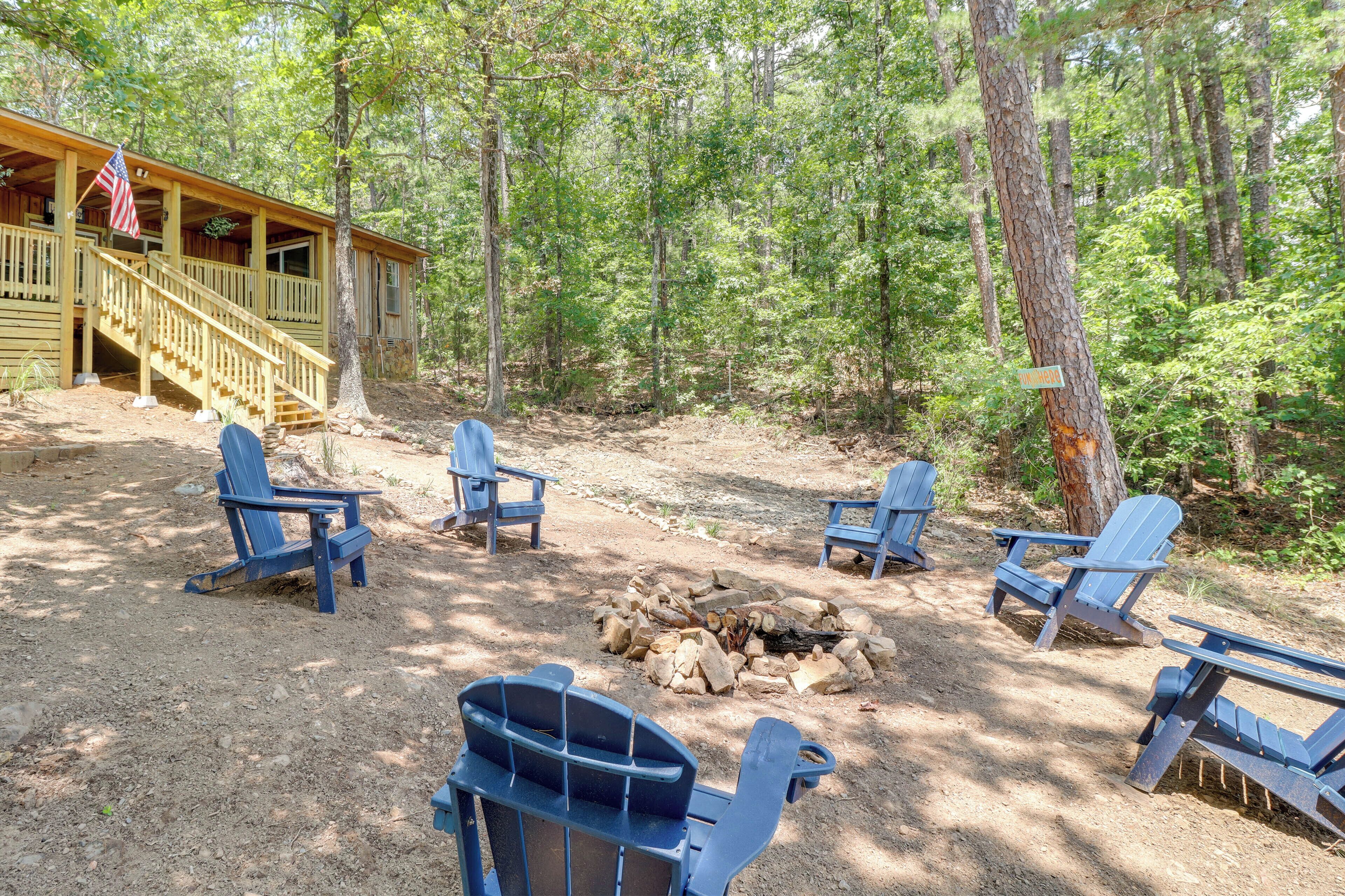 A cabin with a porch and a fire pit surrounded by Adirondack chairs.