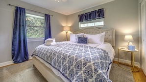 A bedroom with a bed, two bedside lamps, a window with curtains, a ceiling fan, and a small bedside table. - Centrally Located Brevard Home w/ Deck & Fire Pit! (Brevard)