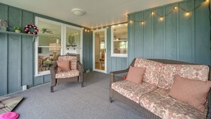 A cozy room with a wicker sofa, a chair, and a small table. There are string lights on the wall and a ceiling fan. - Centrally Located Brevard Home w/ Deck & Fire Pit! (Brevard)