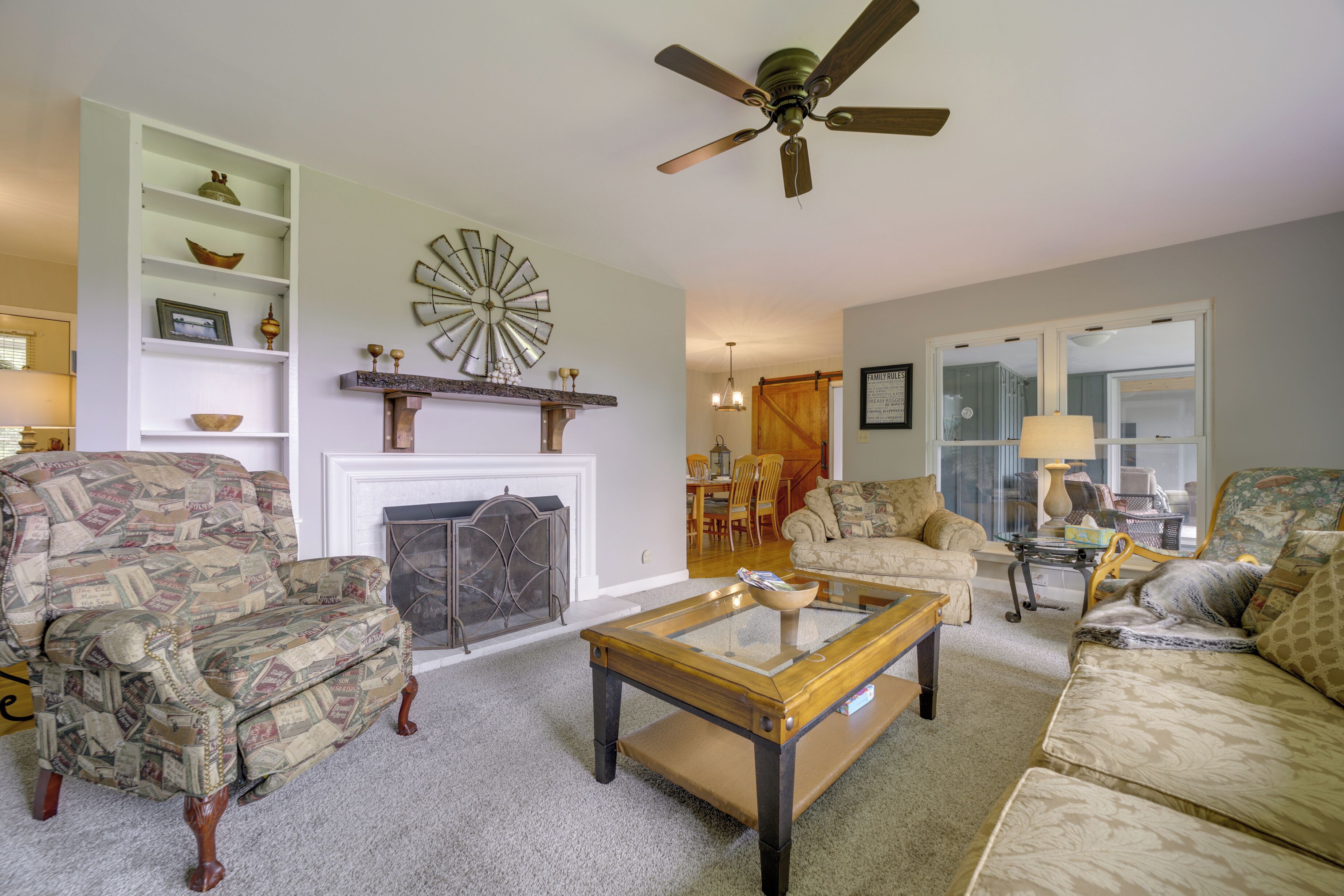 A living room with a fireplace, two armchairs, a sofa, a coffee table, and a ceiling fan.