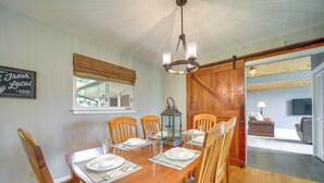A dining room with a wooden table set for six, chairs, a chandelier, and a window with blinds. - Centrally Located Brevard Home w/ Deck & Fire Pit! (Brevard)