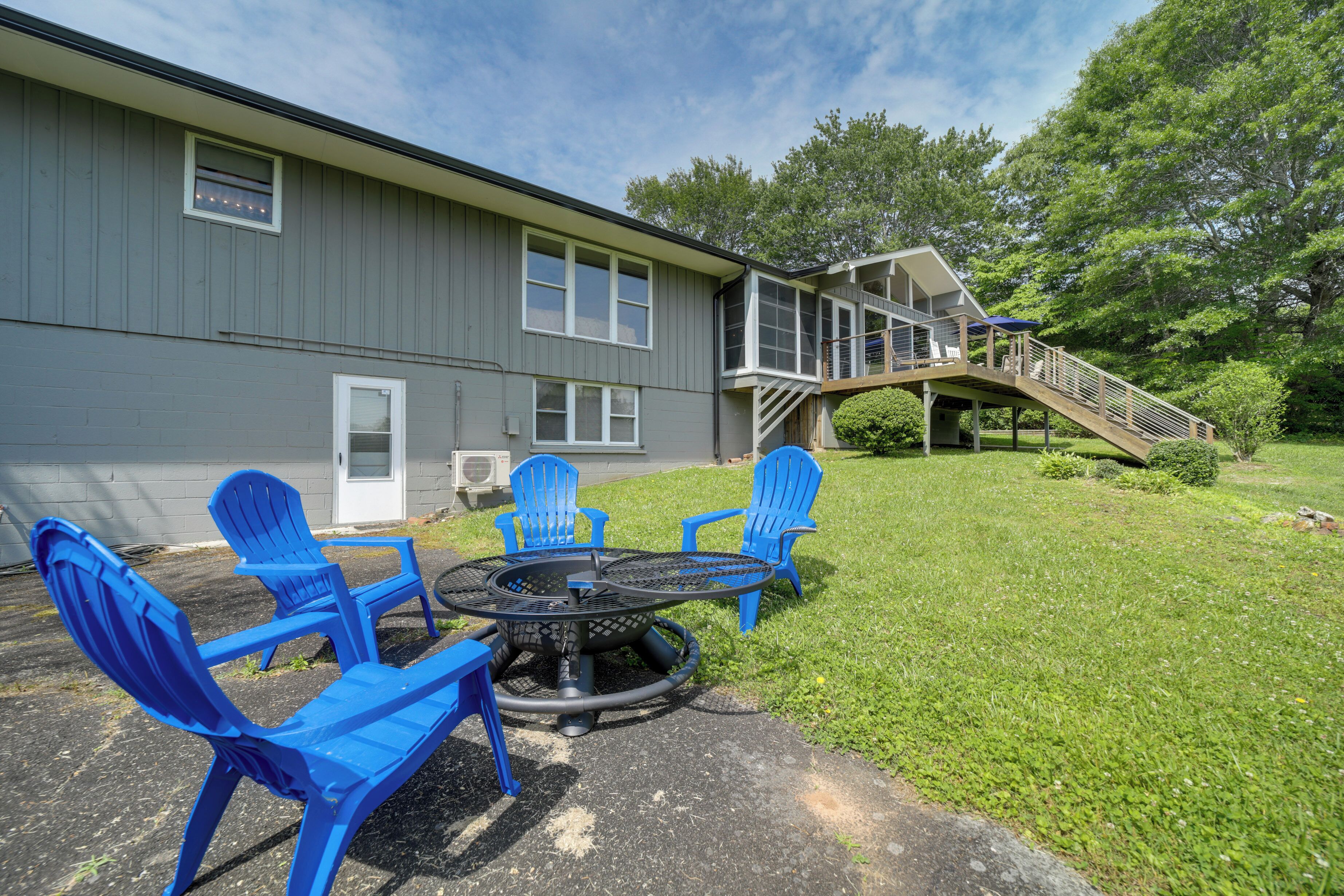 A gray building with a covered patio area featuring a fire pit and blue chairs.