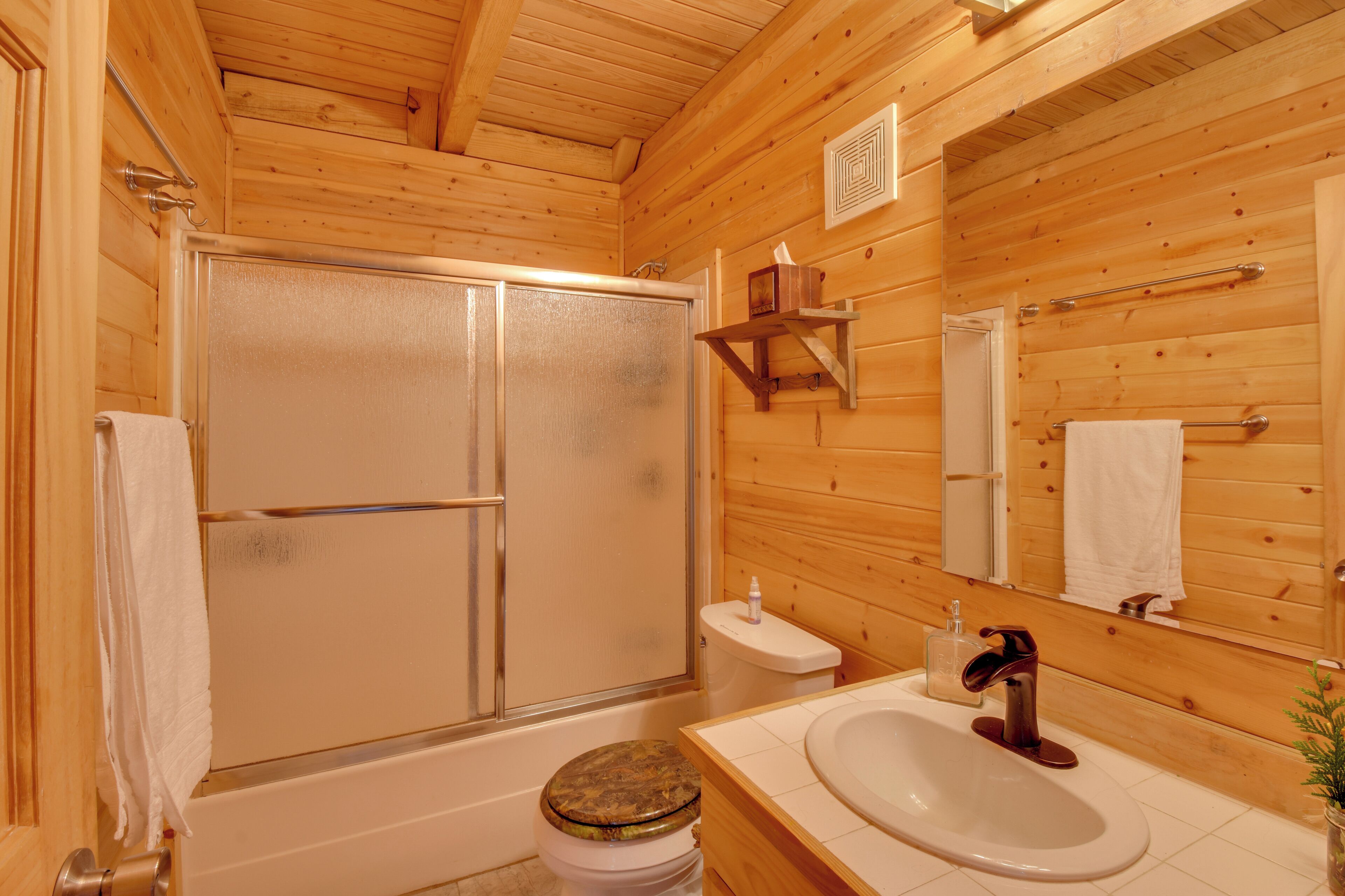A wooden cabin bathroom with a shower, toilet, sink, and a mirror.