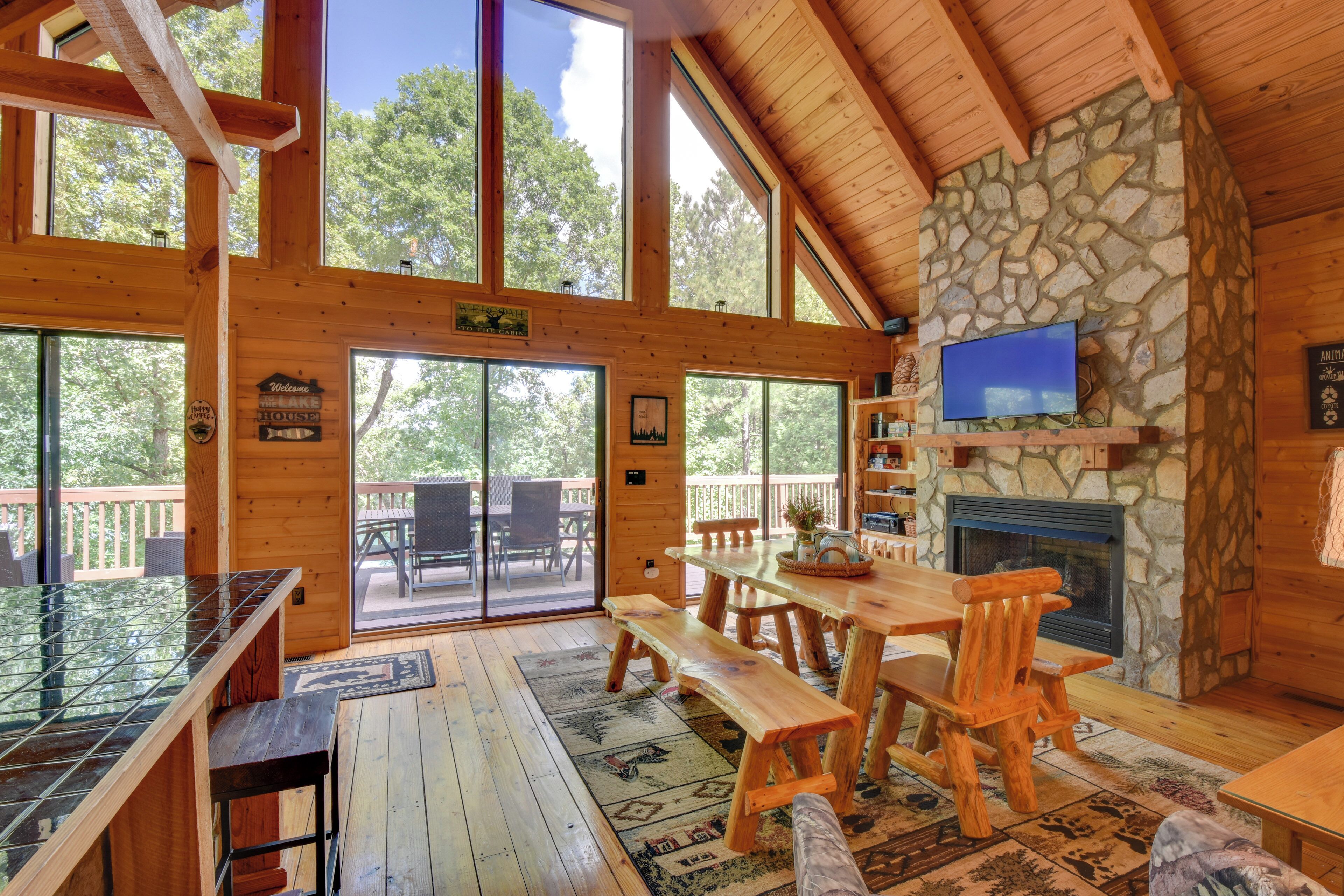 A wooden cabin with a stone fireplace, large windows, and a wooden dining area.