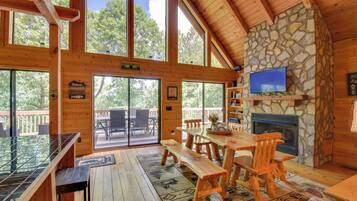A wooden cabin with a stone fireplace, large windows, and a wooden dining area.
