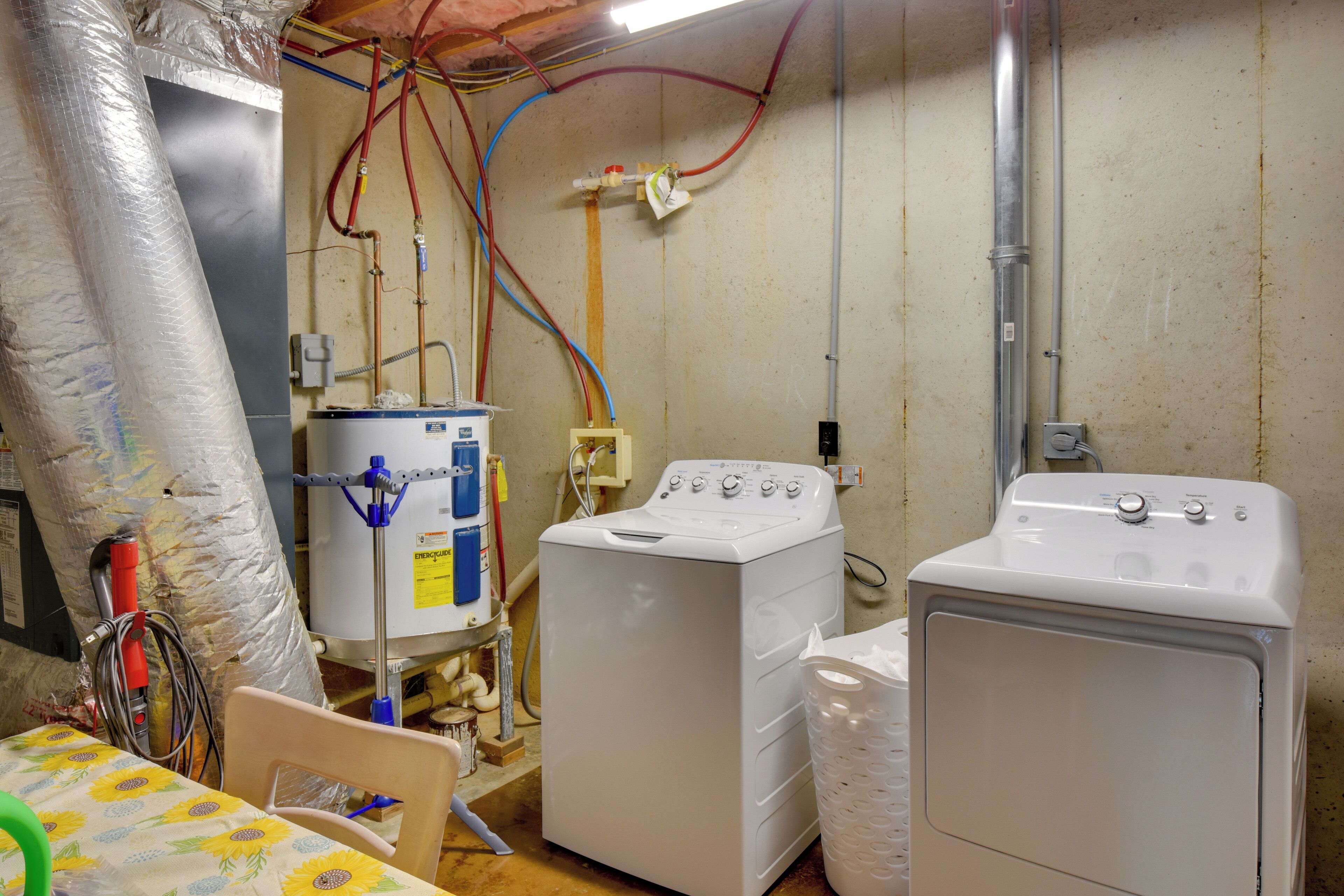 A laundry room with two washing machines, a water heater, and various pipes and hoses.
