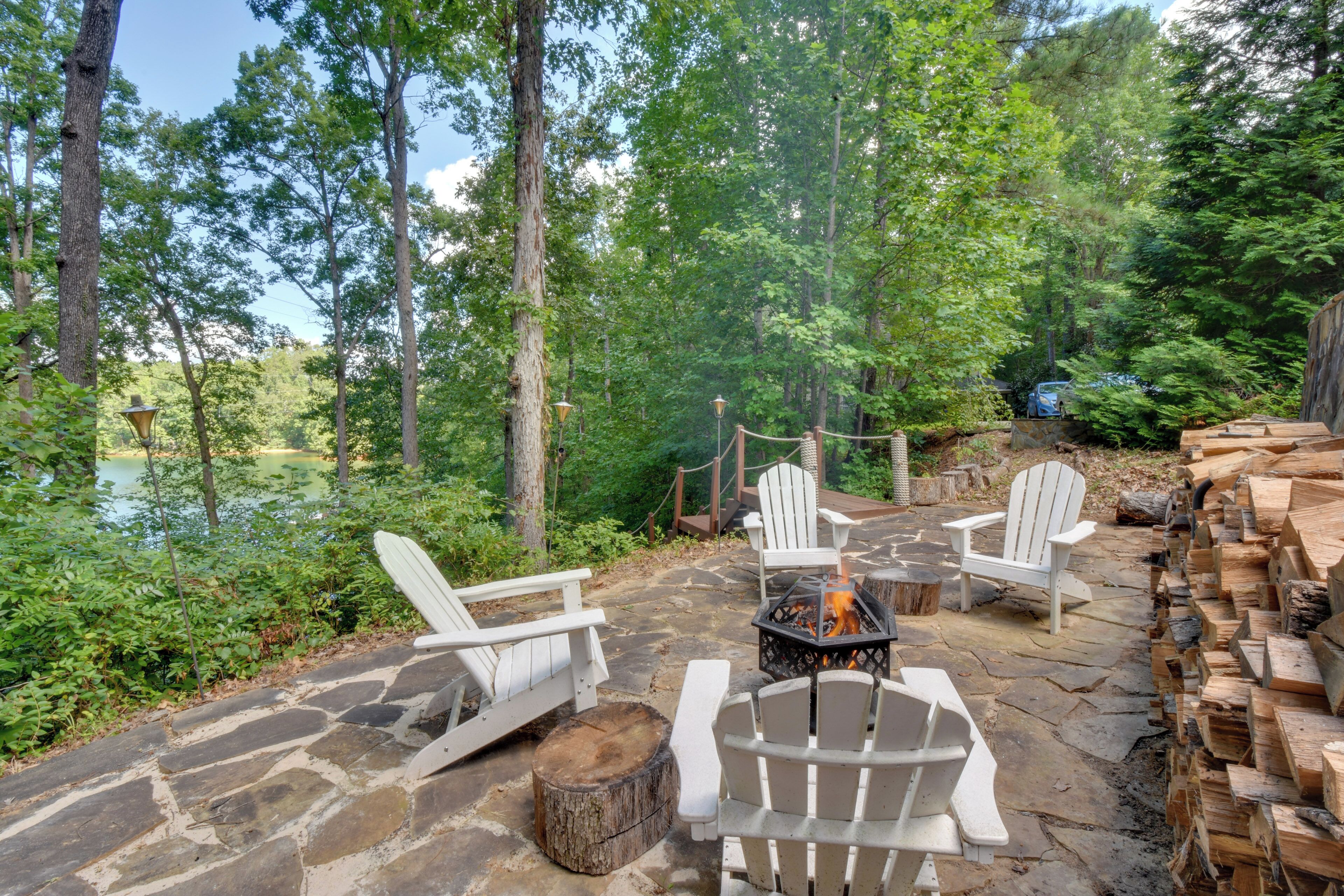 An outdoor seating area with Adirondack chairs and a fire pit, surrounded by stone walls and a forested backdrop.