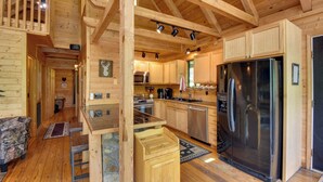 A wooden cabin interior with a kitchen area featuring a stainless steel refrigerator, wooden cabinets, and a stone fireplace. - Lakefront Six Mile Vacation Rental w/ Dock (Six Mile)